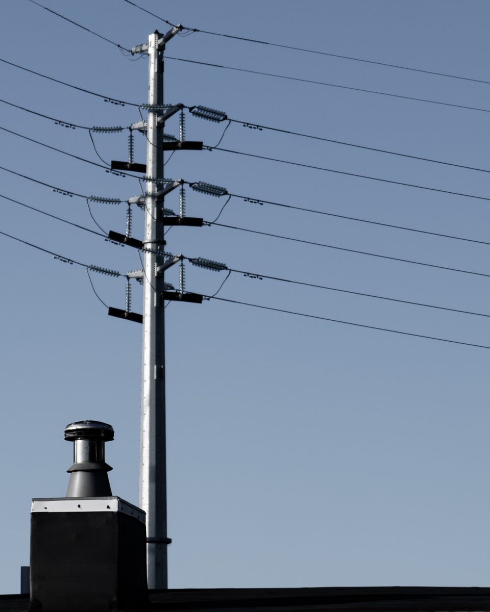 A transmission pole and rooftop vent against blue sky